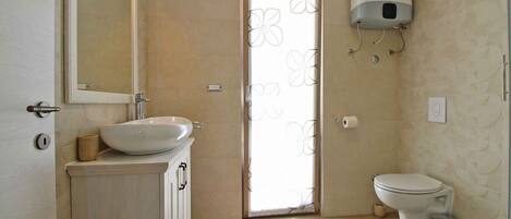 A bathroom with a sink, mirror, toilet, and a shower with a flower-patterned door.