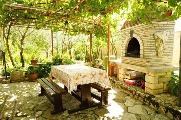 An outdoor patio with a brick oven, wooden benches, and a table with a floral tablecloth.