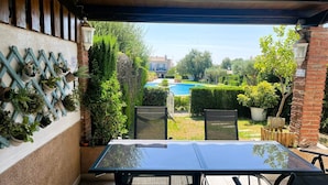 An outdoor patio with a glass table and chairs, a brick wall with potted plants, and a view of a swimming pool and garden. - Villa Conchi (Les Tres Cales)