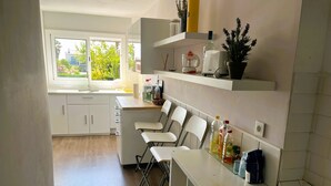 A modern kitchen with white cabinets, a countertop with bar stools, and a window overlooking greenery. - Villa Conchi (Les Tres Cales)