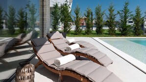 A modern outdoor lounge area with a pool, featuring a curved wooden lounge chair with cushions, a decorative lantern, and a clear view of the surrounding landscape. - Villa Aurum (Zadar)