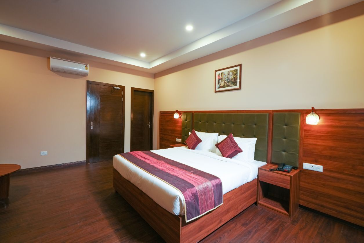 Quarto de hotel com uma cama grande, cabeceira de madeira, mesas de cabeceira e um aparelho de ar condicionado.