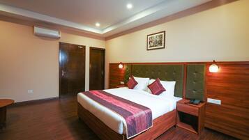 Quarto de hotel com uma cama grande, cabeceira de madeira, mesas de cabeceira e um aparelho de ar condicionado.