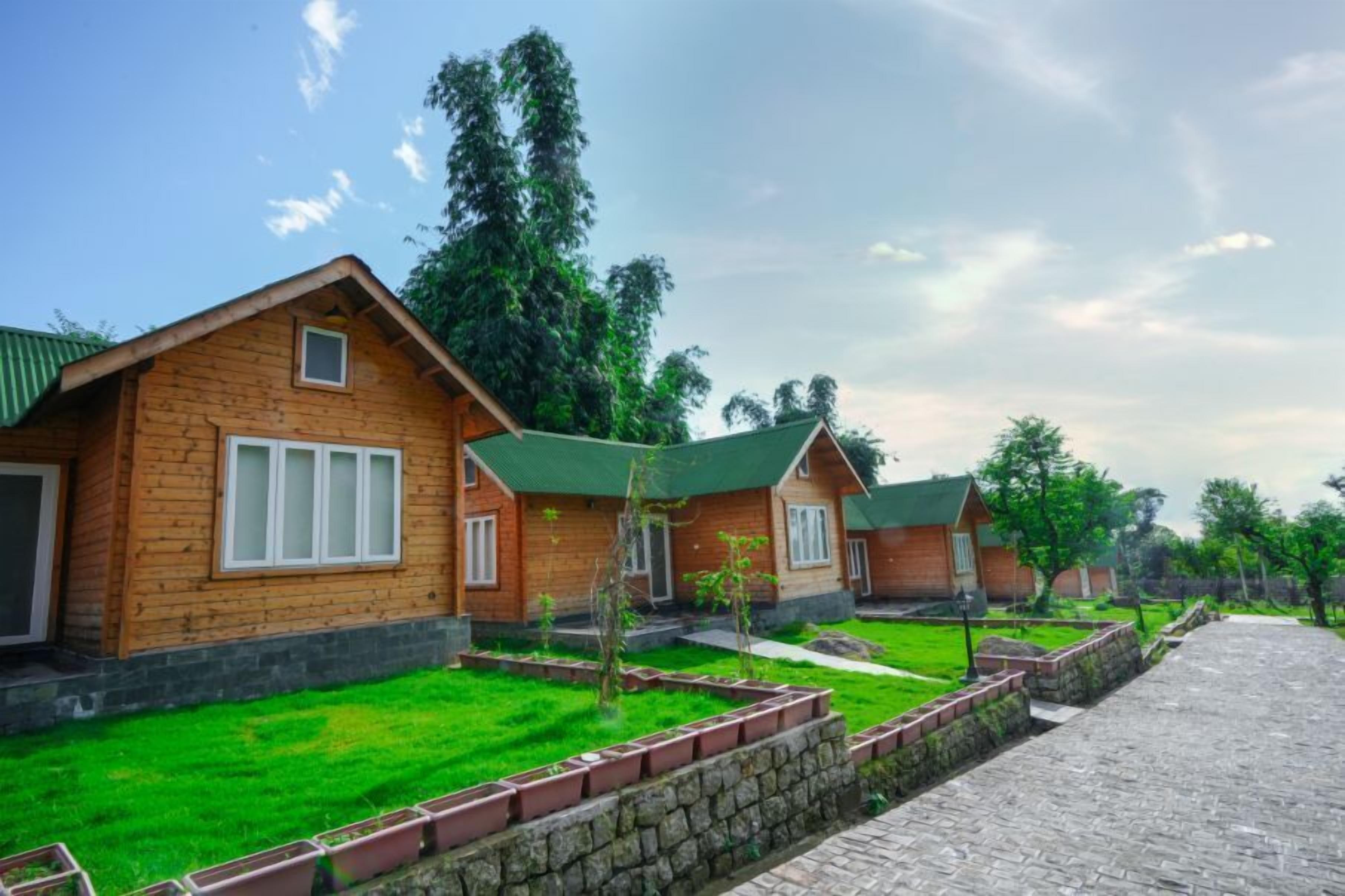 A row of wooden cabins with green roofs, surrounded by well-maintained grass and stone pathways.