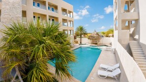 A hotel pool area with a clear view of the pool, lounge chairs, and a palm tree.