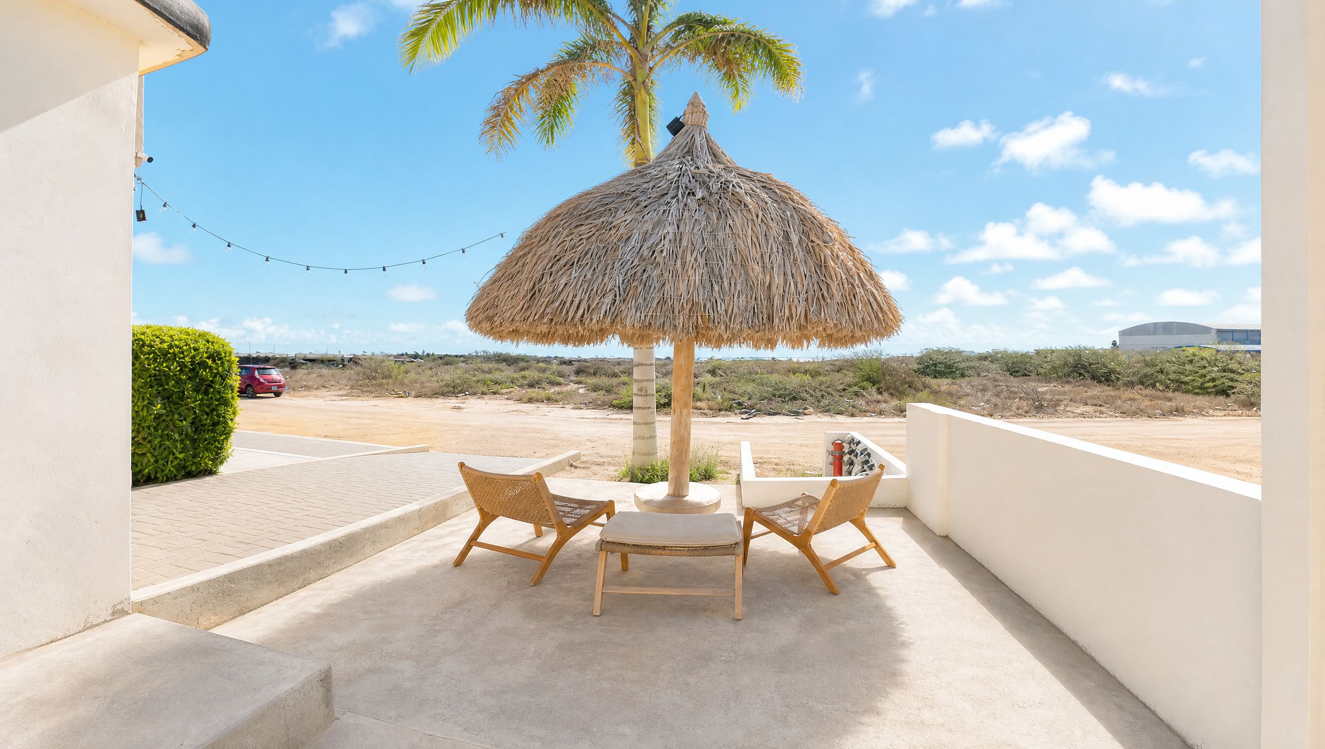 Een terras met een rieten parasol, twee rieten stoelen en een tafel.