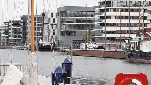 Satamassa on laivoja kiinni laituriin, moderni rakennus, jossa on useita parvekkeita, ja punainen turvallisuusmerkki.