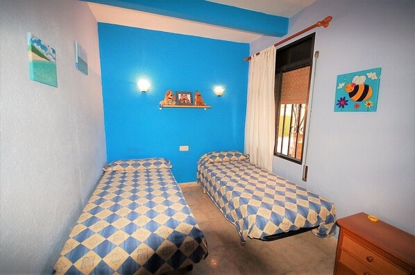 A room with two beds, a window with bars, a shelf with pictures and a dog statue, and a wall with a blue color scheme.