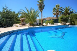 A swimming pool with a dolphin mural, surrounded by palm trees and a building with a balcony.