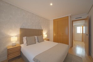 A bedroom with a large bed, two bedside tables with lamps, a wooden wardrobe, and a patterned wall. - Housing Castellana by Sharing Co (Madrid)