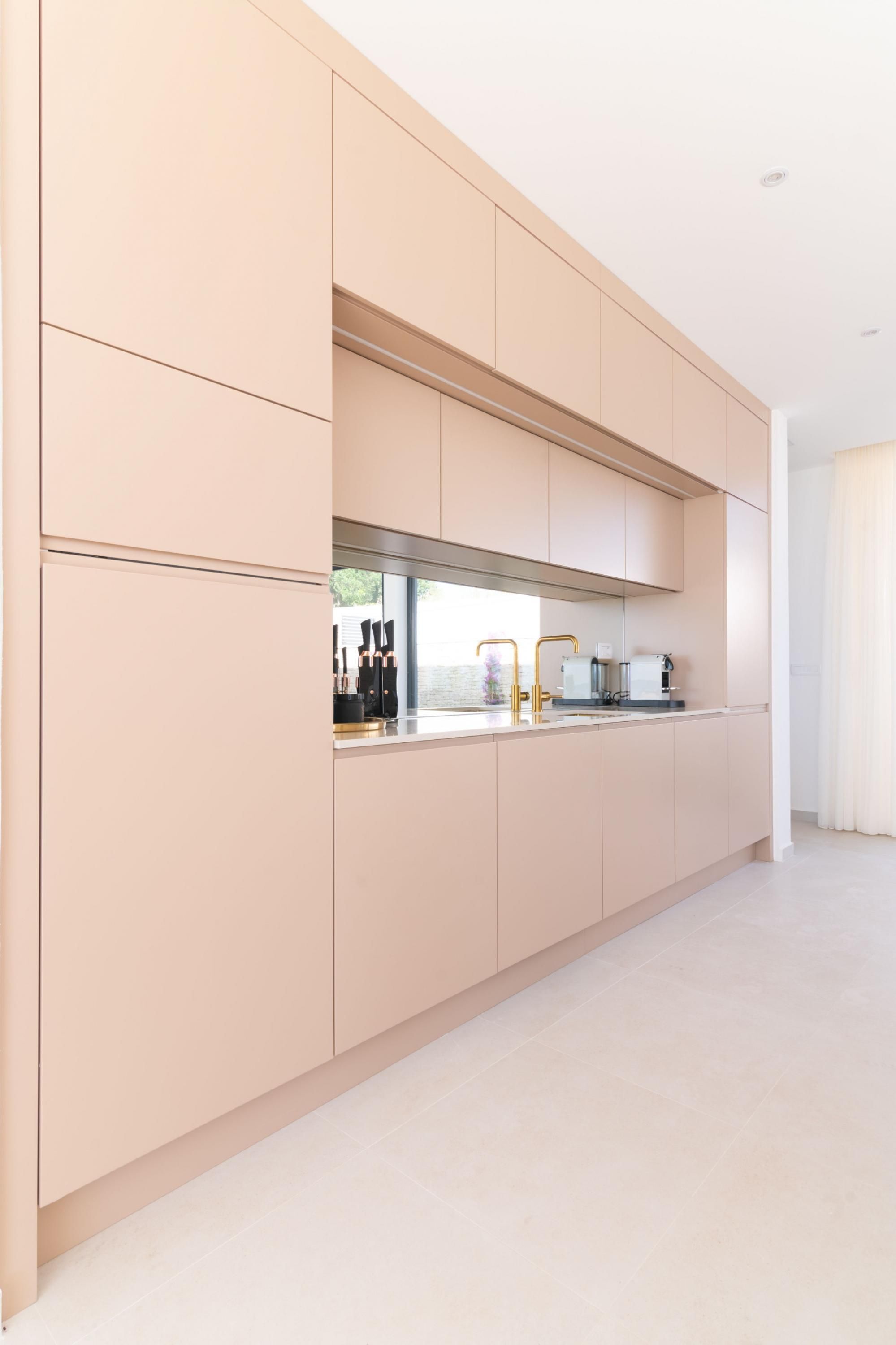 A modern kitchen with light-colored cabinets, a stainless steel range hood, and a countertop with a coffee maker and other appliances.