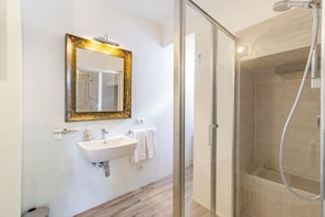 Ein Badezimmer mit einer gläsernen Duschkabine, einem Waschbecken mit Spiegel und einem Handtuch an der Wand.