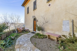 A stone pathway leading to a building with a wooden door and a bench. - Chianti Classico Home Panoramic View (Castellina in Chianti)