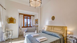 A bedroom with a bed, a chair, a table, and a window with curtains. - Chianti Classico Home Panoramic View (Castellina in Chianti)