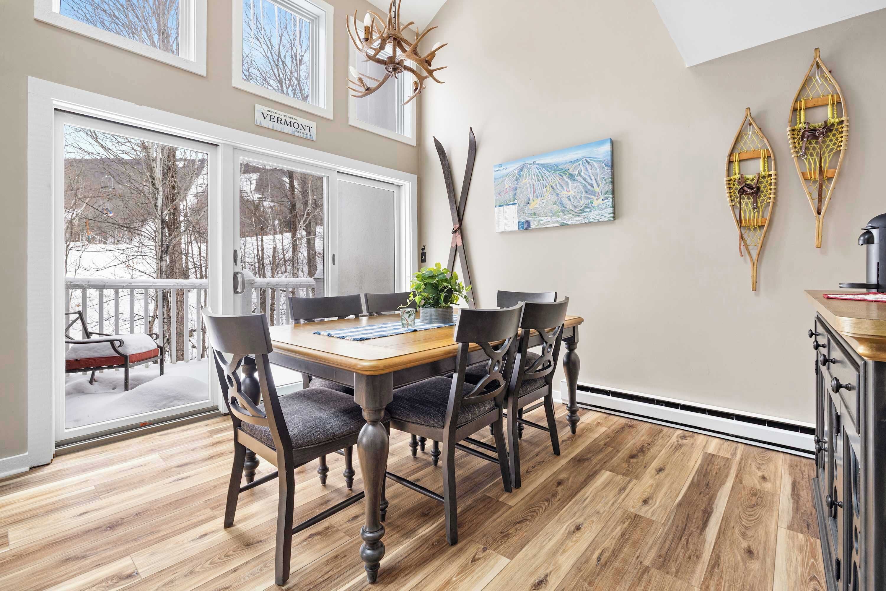 A dining area with a wooden table and chairs, a view through a glass door to a snowy outdoor area, and decorative wall art.