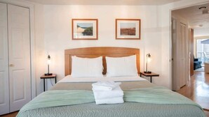 Une chambre d’hôtel avec un grand lit, deux tables de chevet avec des lampes, une tête de lit en bois et deux tableaux encadrés au mur.
