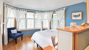 A room with a bed, a chair, a small table, and a window with curtains. - Beautiful backyard, pool, deeded beach rights! (Truro)