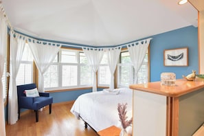 A room with a bed, a chair, a small table, and a window with curtains. - Beautiful backyard, pool, deeded beach rights! (Truro)