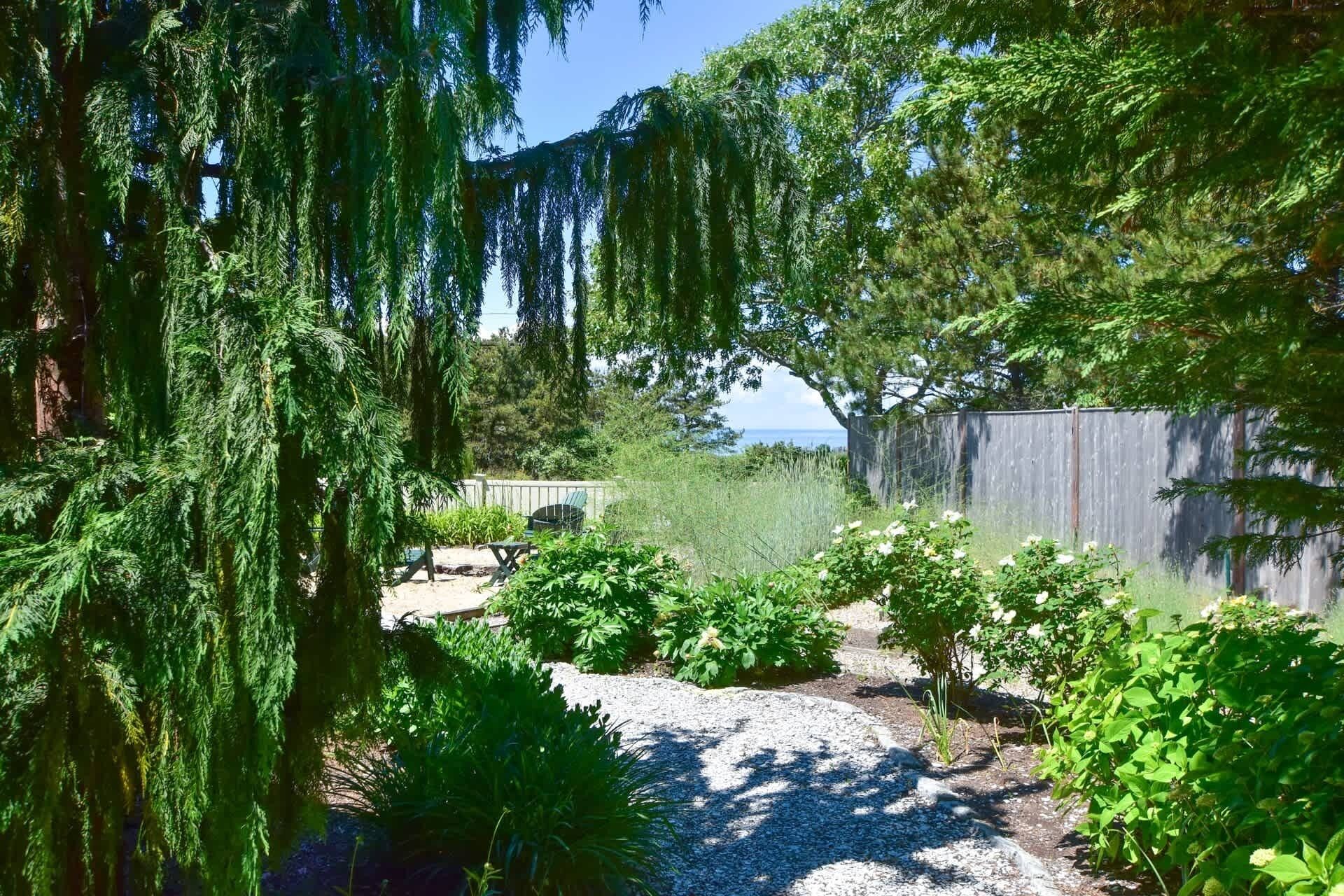 Un jardin avec un chemin de gravier, différentes plantes et une clôture en bois.