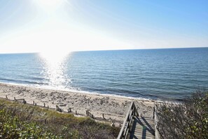 Ein hölzerner Steg führt zu einem Sandstrand mit freiem Blick auf das Meer.