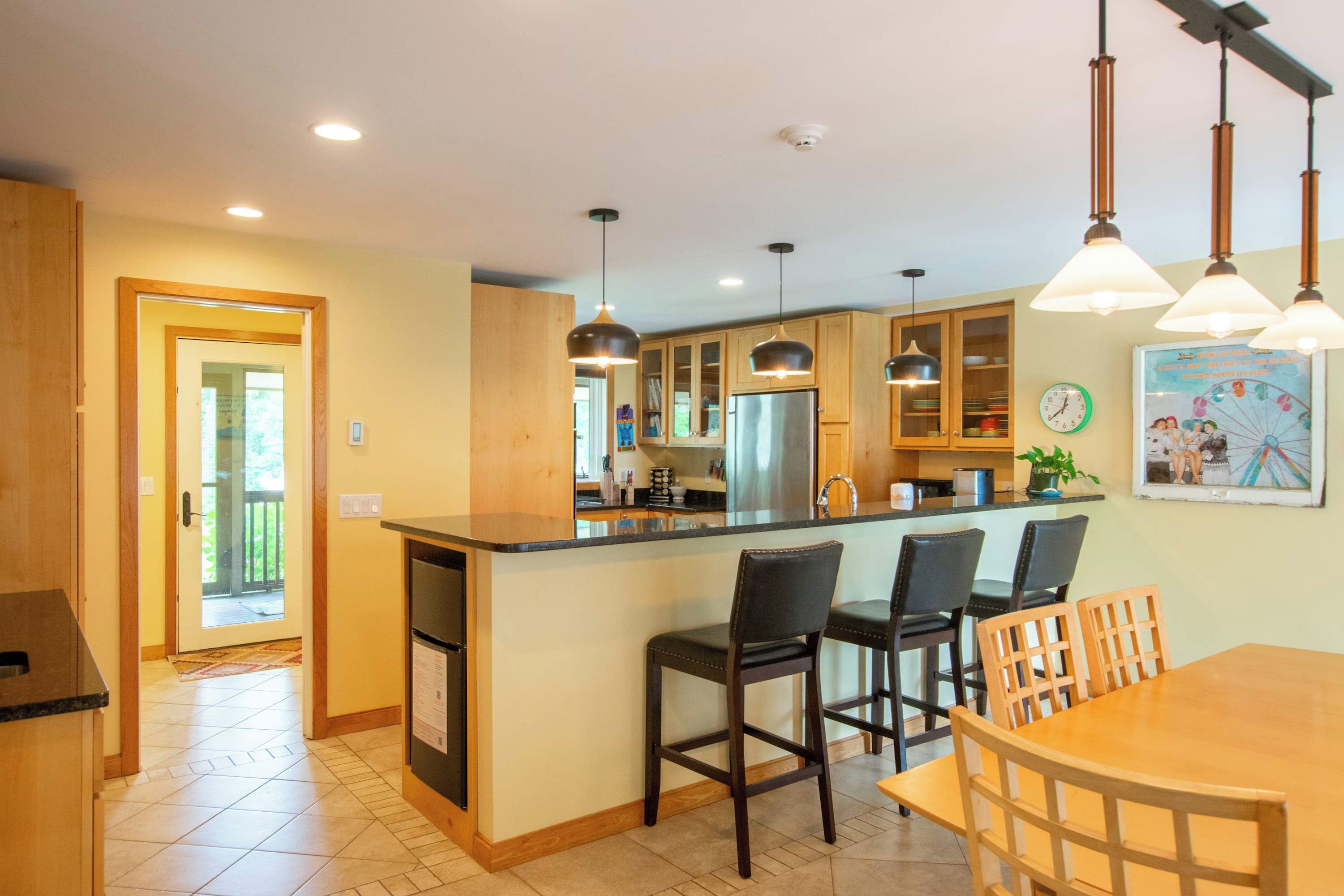 A modern kitchen with a central island, pendant lighting, and a dining area with a wooden table and chairs.