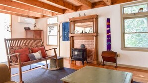 A cozy living room with a wooden bench, a fireplace, and a large window. - Beautiful, private & spacious, great location, large outdoor stone patio! (Wellfleet)