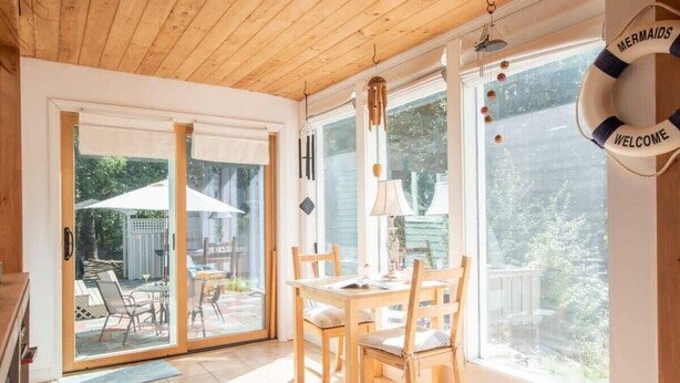 A sunlit room with a wooden ceiling, a dining table with chairs, a large window, and a 'Welcome' sign. - Beautiful, private & spacious, great location, large outdoor stone patio! (Wellfleet)