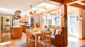 A spacious kitchen with wooden beams, a dining area with a wooden table and chairs, and a large window providing natural light. - Beautiful, private & spacious, great location, large outdoor stone patio! (Wellfleet)