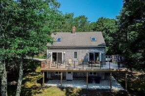 A two-story house with a deck, surrounded by trees.