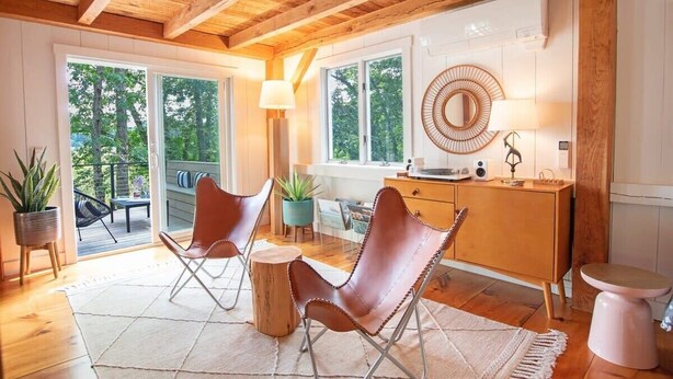 Un interior moderno con vigas de madera, un ventanal grande, un espejo redondo y dos sillones de cuero.