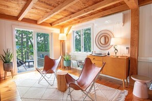 A modern interior with wooden beams, a large window, a round mirror, and two leather chairs. - Eclectic Wellfleet Style Home near Lt. Island! (Wellfleet)