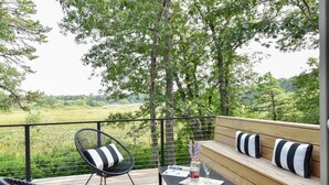 Una terraza con un banco de madera, una silla de mimbre negro y una mesa con una botella y vasos.