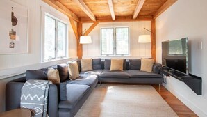 Una sala de estar moderna con un sofá modular, un televisor de pantalla plana y vigas de madera en el techo.