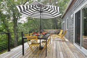 An outdoor deck with a dining table and chairs, surrounded by a wooden deck and a glass railing.