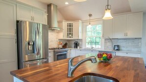 A modern kitchen with white cabinets, stainless steel appliances, a wooden countertop, and a large window. - Roof Deck, Walk to Forest Beach, Fire Pit! (Chatham)