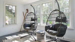 A room with two black hanging chairs, a small round ottoman, and a ceiling fan. - Roof Deck, Walk to Forest Beach, Fire Pit! (Chatham)