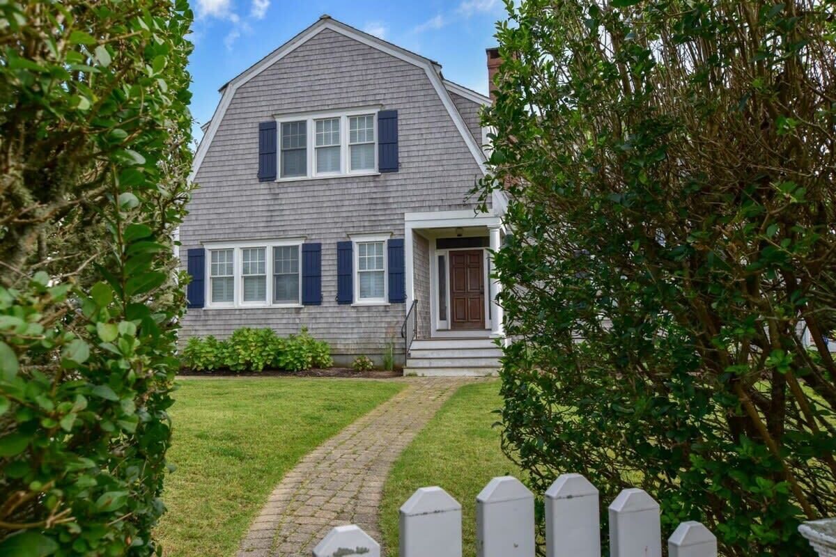 A two-story house with a grey exterior and dark shutters, a front porch, and a brick pathway leading to the entrance.