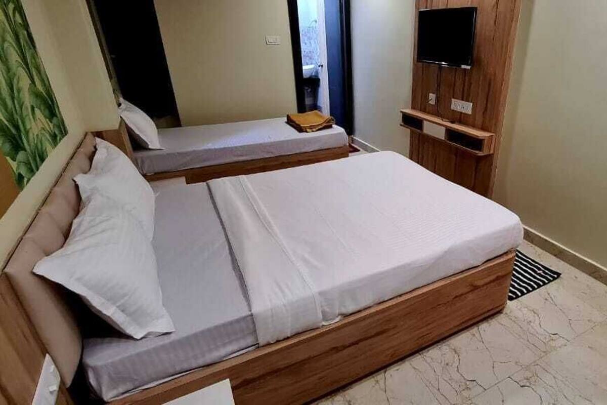 A small, compact room with two single beds, a wooden wardrobe, and a television on a wooden stand.