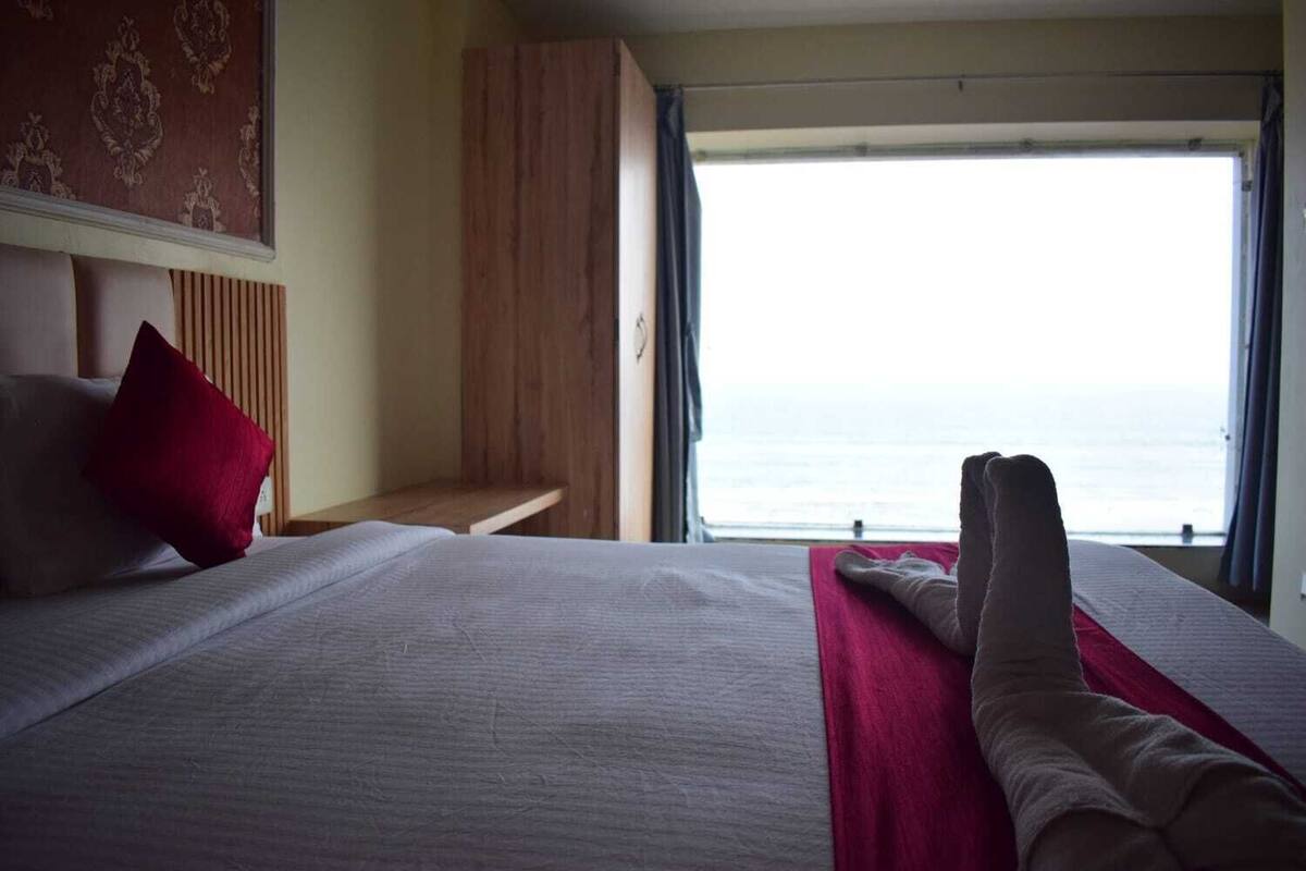 A hotel room with a bed, a wooden bench, and a view of the sea.