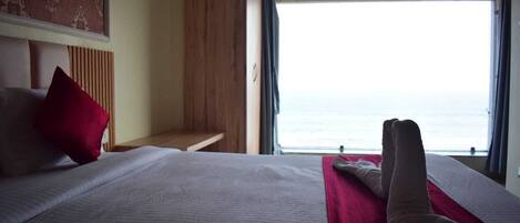 A hotel room with a bed, a wooden bench, and a view of the sea.