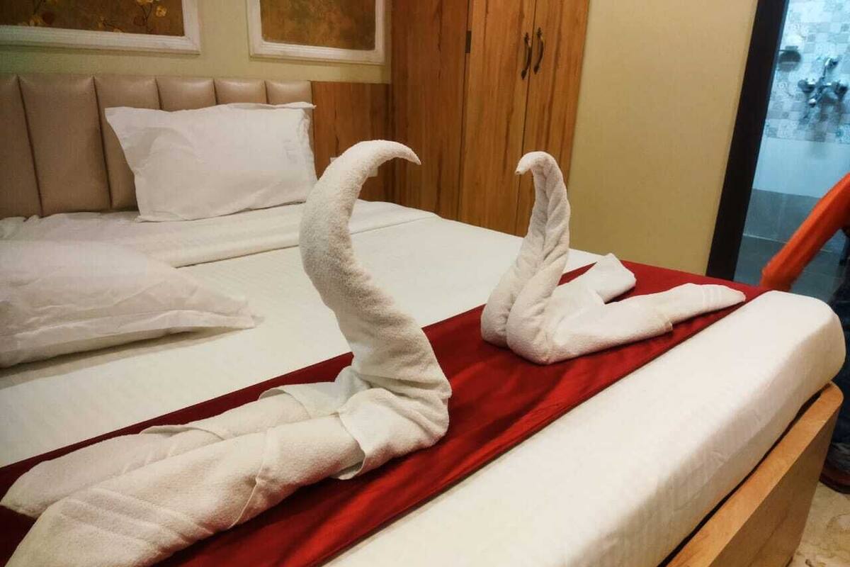 A hotel room with a bed, a red blanket, and two towels arranged in a swan shape.