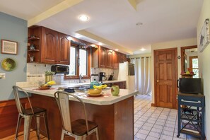 A kitchen with wooden cabinets, a central island with stools, a refrigerator, and a microwave.