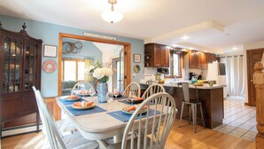 Un comedor con una mesa dispuesta para cuatro, una cocina con armarios de madera y un espejo decorativo con un cartel arriba.