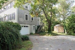 A two-story house with a garage, a wooden shed, and a tree in front.