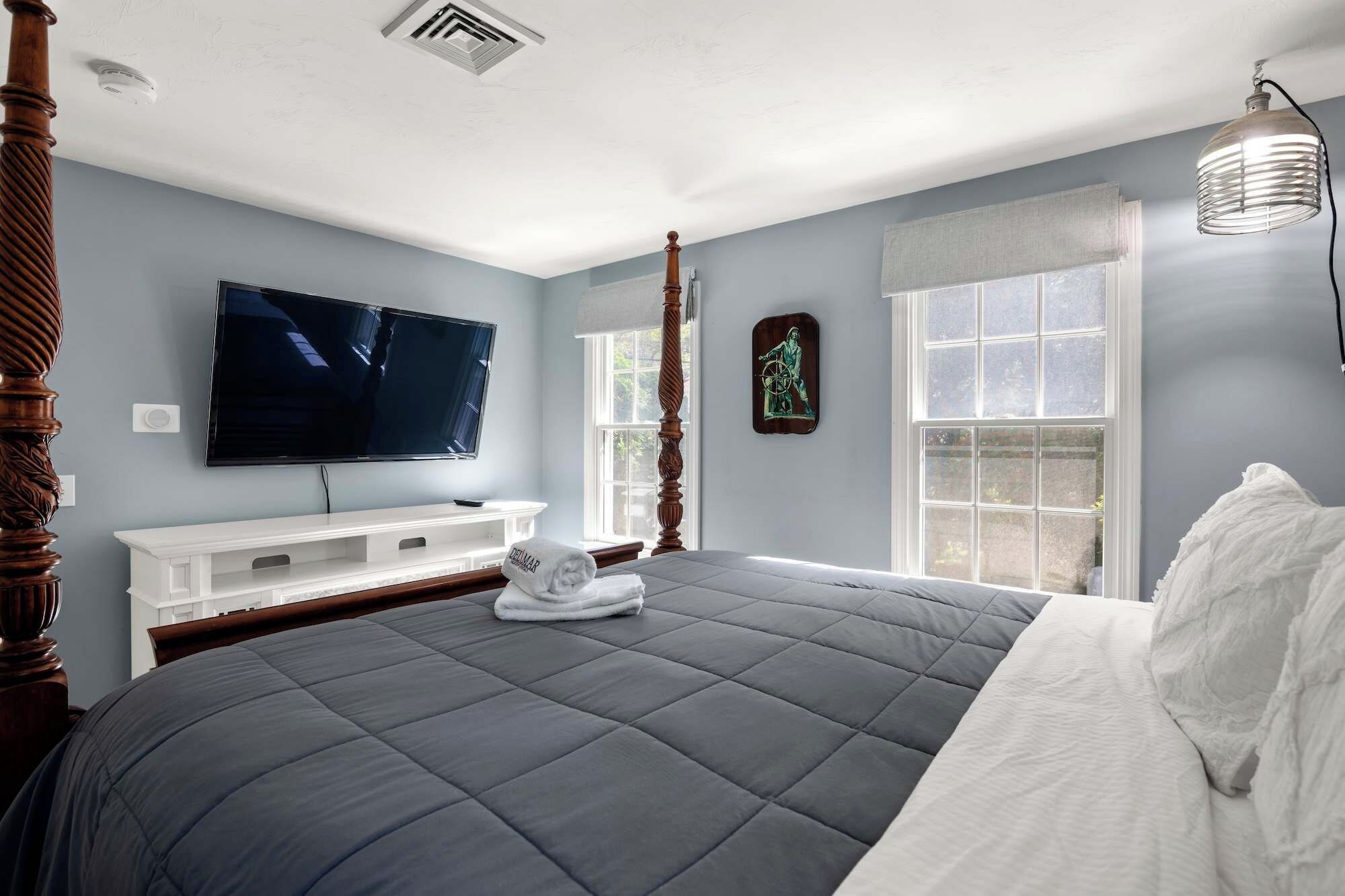 Un dormitorio con una cama grande, un televisor en la pared y un ventanal con cortinas.