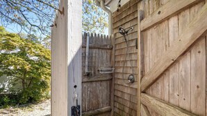 A wooden outdoor shower with a metal hose, a metal rack, and a small shelf. - Hot Tub, 200 ft to Beach! (Dennis)