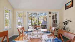A dining area with a wooden table set for six, surrounded by chairs, with a view of the outdoors through a glass door. - Hot Tub, 200 ft to Beach! (Dennis)