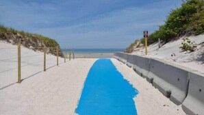 Un sentier menant à une plage avec une piscine bleue, une plage de sable et un panneau indiquant une zone protégée.