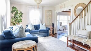 Un salon spacieux avec un canapé bleu, une table ronde en osier et un escalier doté d’une rampe en bois.