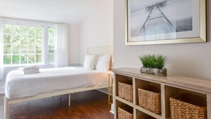 Une chambre à coucher avec un lit, une fenêtre, un tableau encadré et des paniers en osier sur une étagère.